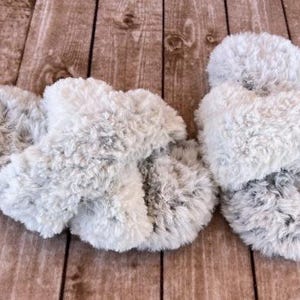 May include: A pair of gray fuzzy slippers with a criss-cross strap design.