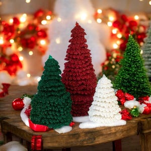 May include: A selection of glitter-covered Christmas trees in different sizes and colours. The trees are in shades of green, red, and white. They are arranged on a wooden surface, with festive decorations in the background, creating a holiday scene.