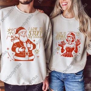 Puede incluir: Dos sudaderas beige con diseños navideños. Una presenta a Papá Noel con el texto "I love to stuff her stocking". La otra muestra a una mujer con campanas y el texto "I love to jingle his bells."