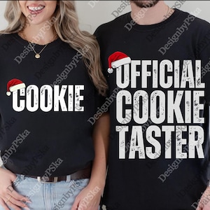 May include: Black t-shirts with white text and a Santa hat graphic. One shirt reads "COOKIE" and the other reads "OFFICIAL COOKIE TASTER". A festive holiday theme.