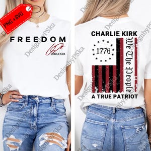 May include: White t-shirt with the word "FREEDOM" in black, and a signature that says "Charlie Kirk". The back of the shirt features a distressed American flag design with the text "CHARLIE KIRK", "1776", "We The People", and "A TRUE PATRIOT".