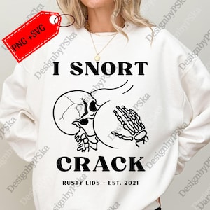 May include: White sweatshirt with a black graphic that says "I SNORT CRACK" with a skull and skeleton hand design. The text "RUSTY LIDS - EST. 2021" is below the graphic. The sweatshirt has a crew neck and long sleeves.