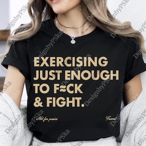May include: Black t-shirt with the text "EXERCISING JUST ENOUGH TO F*CK & FIGHT." in a gold color. The shirt also has the text "Not for pussies" and "Frased" in a smaller font.