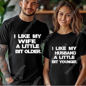 K&ouml;nnte beinhalten: Zwei passende schwarze T-Shirts mit wei&szlig;em Text. Eines lautet "I LIKE MY WIFE A LITTLE BIT OLDER." Das andere lautet "I LIKE MY HUSBAND A LITTLE BIT YOUNGER." F&uuml;r Paare.