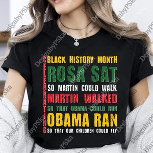 May include: Black t-shirt with the text "BLACK HISTORY MONTH" and a quote about Rosa Parks, Martin Luther King Jr., and Barack Obama. The text is in green, red, yellow, and white.
