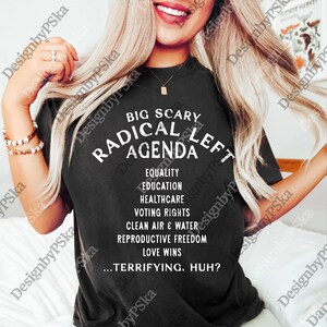 Puede incluir: Camiseta negra con texto blanco. El texto dice "BIG SCARY RADICAL LEFT AGENDA" seguido de una lista de ideales políticos. La camiseta también incluye la frase "...TERRIFYING, HUH?"