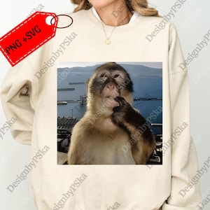 Peut inclure: Sweat-shirt beige avec une image carrée d'un singe pensif, sur fond de paysage marin. L'image comprend le texte "PNG + SVG" sur une étiquette rouge.