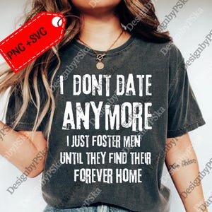 May include: Dark grey t-shirt with the text "I DON'T DATE ANYMORE I JUST FOSTER MEN UNTIL THEY FIND THEIR FOREVER HOME" in white. A red tag with "PNG + SVG" is in the upper left corner.