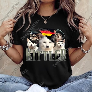 May include: Black t-shirt featuring a graphic of five cats, each wearing a different military-style hat. The cats are arranged in front of a German flag. The word "KITTLER" is printed in large, stylized letters below the cats.