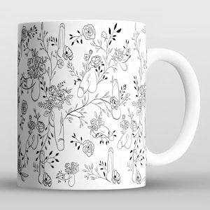 以下が含まれることがあります： 白のセラミックマグ。黒と白の花柄で、男性器のイメージが描かれています。デザインには、ペニスと花の様式化されたイラストが含まれており、ユーモラスなパターンを作成しています。マグには白いハンドルが付いています。