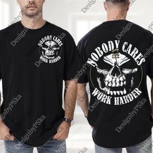 Op de afbeelding: Zwart t-shirt met een schedelontwerp en de tekst "NOBODY CARES WORK HARDER". Het ontwerp is wit en goudkleurig. Het ontwerp is gedrukt op de voor- en achterkant van het shirt.