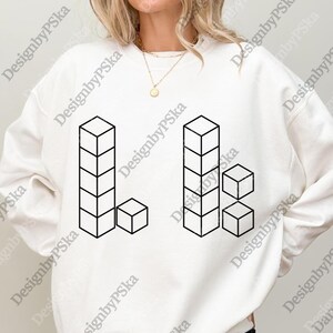 May include: White sweatshirt featuring a black geometric design of stacked cubes. The design includes two vertical stacks of cubes and several individual cubes. The sweatshirt has a crew neck and long sleeves.