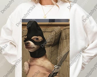 May include: A white sweatshirt featuring a humorous image of a small dog wearing a black ski mask and holding a knife. The dog is sitting on a couch. The image has the text "DesignbyPSka" repeated around the image.