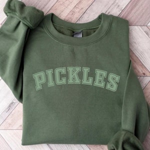 May include: A green sweatshirt with the word "PICKLES" printed in a white, outlined font.