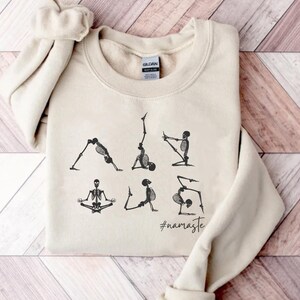 May include: A beige sweatshirt with a graphic of skeletons doing yoga poses. The text "#namaste" is printed below the skeletons.