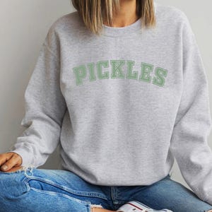 May include: A gray sweatshirt with the word "PICKLES" printed in green on the front.