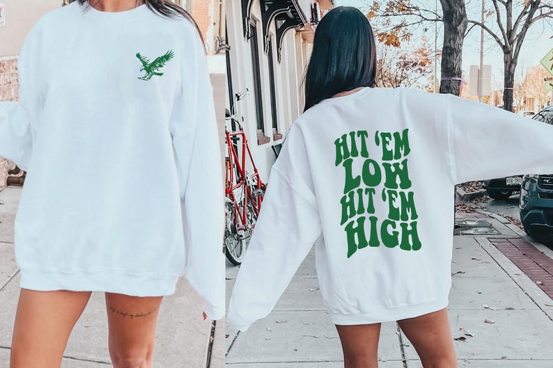 K&ouml;nnte beinhalten: Zwei wei&szlig;e Sweatshirts mit gr&uuml;nem Text und Grafiken. Ein Sweatshirt hat eine gr&uuml;ne Adlergrafik auf der Vorderseite. Das andere Sweatshirt hat den Text "Hit 'em Low Hit 'em High" auf der R&uuml;ckseite.