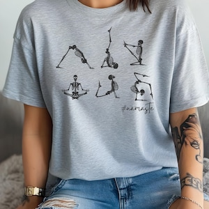May include: A light gray t-shirt with a graphic of skeletons doing yoga poses. The text "#namaste" is printed below the skeletons.