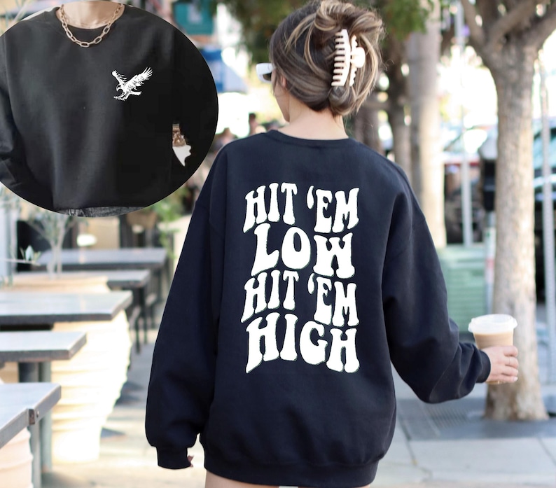 K&ouml;nnte beinhalten: Schwarzer Pullover mit wei&szlig;em Text "Hit 'em Low Hit 'em High" auf der R&uuml;ckseite. Der Pullover hat eine lockere Passform und lange &Auml;rmel.