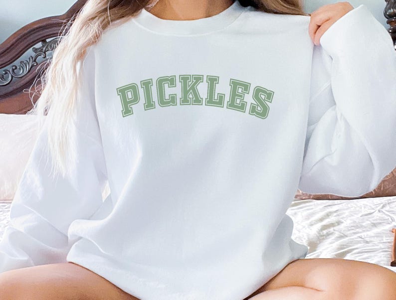 May include: White sweatshirt with the word "PICKLES" printed in green letters with a varsity style font.