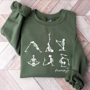 May include: A green sweatshirt with a white graphic of skeletons doing yoga poses. The text "#namaste" is printed below the skeletons.