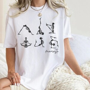May include: White t-shirt with a graphic of skeletons doing yoga poses. The text "#namaste" is printed below the skeletons.