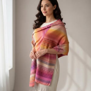 May include: A colorful shawl with a gradient of pink, orange, and yellow hues. The shawl features a patterned design with fringe at the bottom. The woman is wearing a white dress.