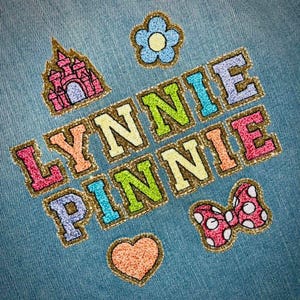 May include: A denim jacket with colorful embroidered patches. The patches include a castle, a flower, a bow, a heart, and the words "LYNNIE PINNIE".