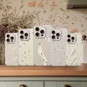 Peut inclure: Cinq coques de téléphone beiges avec un motif de piste de ski. Chaque coque présente une taille différente et une illustration unique de skieurs sur une montagne enneigée. Les coques sont disposées sur une surface en bois devant un papier peint floral.