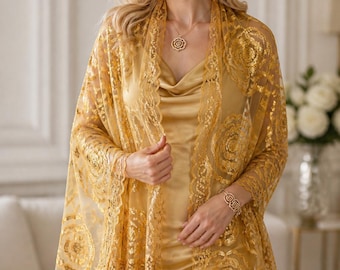 May include: A woman wearing a gold-colored lace shawl with a floral pattern and fringe. She is also wearing a matching gold dress, necklace, earrings, and bracelet. The shawl is draped over her shoulders.