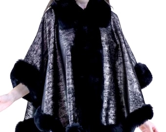 May include: A metallic silver and black cape with a black fur collar and trim. The cape has a flowing design and is worn over the shoulders. The fur trim is around the collar, cuffs, and bottom hem.
