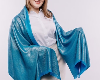 May include: A woman wearing a white shirt and a light blue shimmery scarf. She is wearing a beige skirt and black shoes with gold chains.
