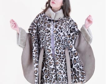 Könnte beinhalten: Ein Umhang mit Leopardenmuster und einem beigefarbenen Kragen und Besatz. Der Umhang hat einen Knopfverschluss und zwei beige Bindegürtel. Die Ärmel sind einfarbig beige. Der Umhang wird über einem weißen Oberteil und einer weißen Hose getragen.