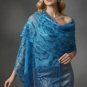 May include: A sheer, light blue shawl with intricate sequin and embroidered detailing. The shawl features a floral pattern and fringe along the bottom edge. The garment is draped over the shoulders.