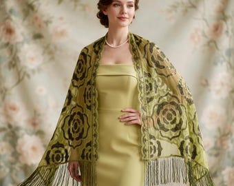 May include: A woman wearing a light green dress and a matching sheer shawl. The shawl is decorated with black floral patterns and fringe. The background features a floral pattern.