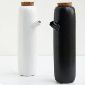 Pode incluir: Duas garrafas de óleo de cerâmica, uma branca e outra preta, cada uma com uma rolha de cortiça e um bico. As garrafas têm um design minimalista e são adequadas para uso na cozinha. A garrafa branca está à esquerda e a preta à direita.