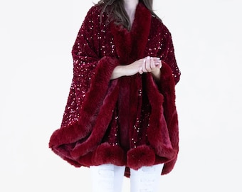 May include: A burgundy sequined cape with a faux fur trim. The cape is worn over white jeans.