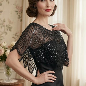 May include: A black sleeveless dress paired with a sheer black capelet featuring intricate black beadwork and sequin embellishments in a leaf-like pattern. The capelet has a scalloped hemline and covers the shoulders and upper chest area.