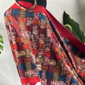 Könnte beinhalten: Ein rot-blauer Schal mit geometrischem Muster. Der Schal ist aus weichem, leichtem Stoff und hat einen Fransenrand.