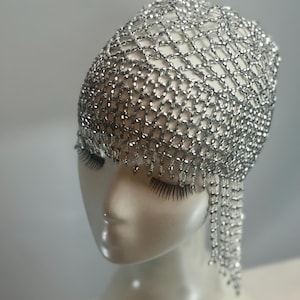 May include: A silver beaded headpiece with a net design and dangling strands. The headpiece is worn on a white mannequin head.