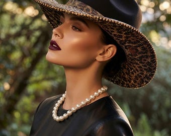 Puede incluir: Un sombrero fedora negro con ala ancha de estampado de leopardo en tonos marrón y negro, junto a un collar de perlas blancas. El sombrero presenta una copa estructurada y una banda oscura que separa la parte superior negra de la ala estampada.