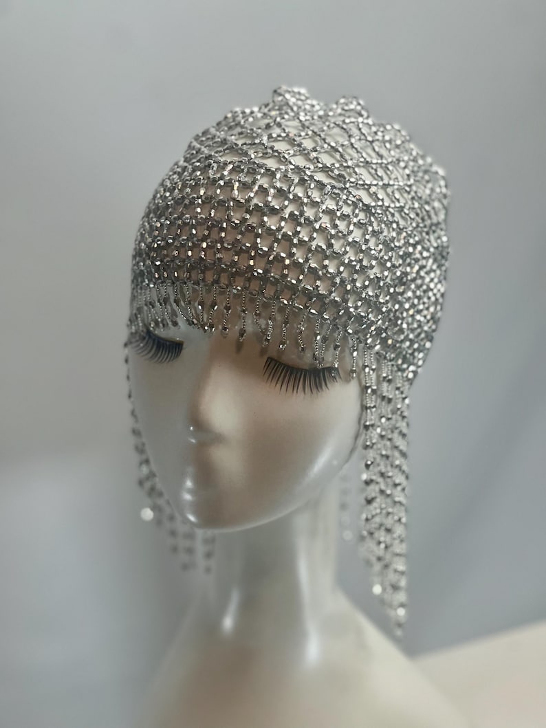 May include: A silver beaded headpiece with a chainmail design and dangling strands of beads.
