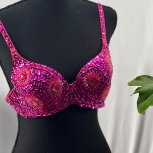 Op de afbeelding: Een roze, met pailletten bezette bh met een bloemenpatroon. De bh is op een zwart mannequin.
