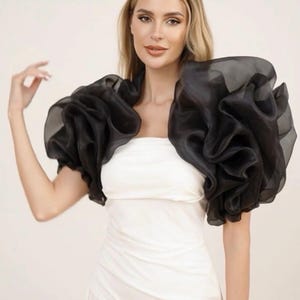 May include: Black organza shoulder wrap with voluminous, ruffled sleeves. The sheer fabric creates a dramatic effect, adding a touch of elegance. This accessory is designed to be worn over a strapless or sleeveless top.