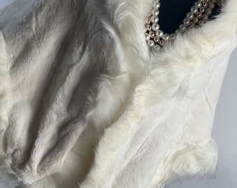 May include: White faux fur shawl with a fluffy texture and a soft, luxurious feel. The shawl is trimmed with a thick, white fur border.