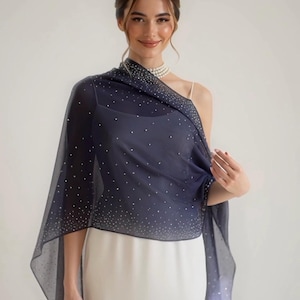 May include: A navy blue sheer shawl with scattered silver-colored embellishments. The shawl is draped over the shoulders and arms. The garment is worn over a white dress.