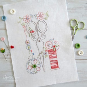 May include: Embroidered design on white linen fabric featuring a pair of scissors, a spool of red thread, and a pincushion with a flower design. The design is surrounded by small flowers and leaves.