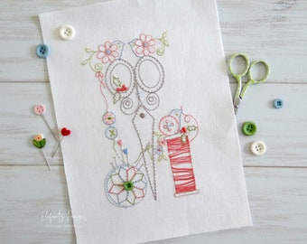 May include: Embroidered design on white linen fabric featuring a pair of scissors, a spool of red thread, and a pincushion with a flower design. The design is surrounded by small flowers and leaves.