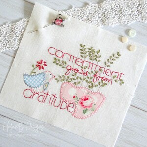 May include: Embroidered fabric panel with the text "Contentment grows from gratitude" in red thread. The panel features a blue bird with a red flower, green leaves, and two pink hearts with a floral pattern.