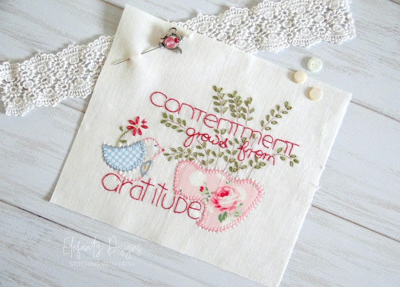 May include: Embroidered fabric panel with the text "Contentment grows from gratitude" in red thread. The panel features a blue bird with a red flower, green leaves, and two pink hearts with a floral pattern.